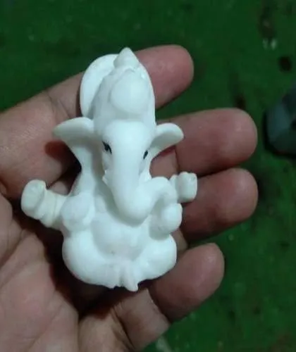 A miniature, unpainted marble-finish Ganesha idol held in hand to show its small scale and fine sculpting details.