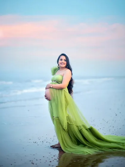 A stunning solo portrait of the mother-to-be against the serene backdrop of the sea and a pastel sky.