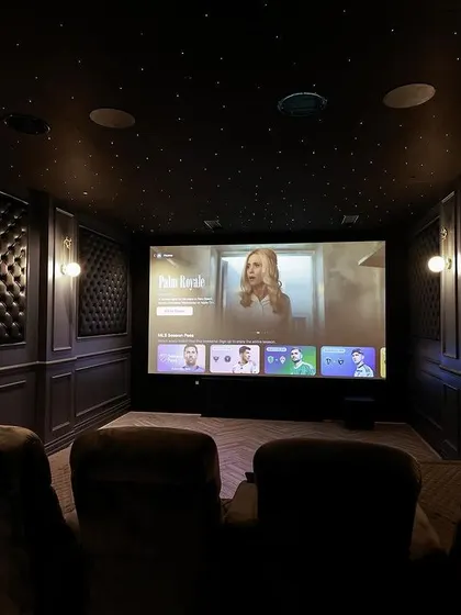 The screen is ready for action in this elegant theater. The dark, tufted panels on the walls are not just for looks; they are crucial for absorbing sound and preventing reflections.