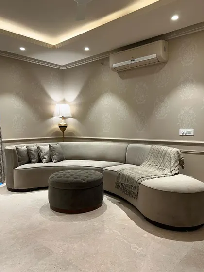 A custom-designed curved sectional sofa fits perfectly into this corner, maximizing seating while maintaining a soft, elegant look. The tufted ottoman adds another layer of texture and comfort.