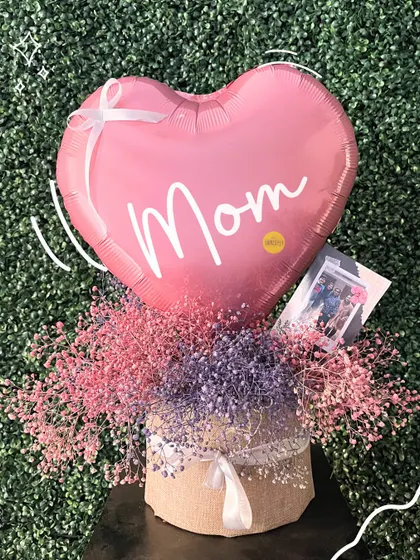 A delicate Mother's Day gift box filled with colorful dried baby's breath and a simple "Mom" heart balloon.