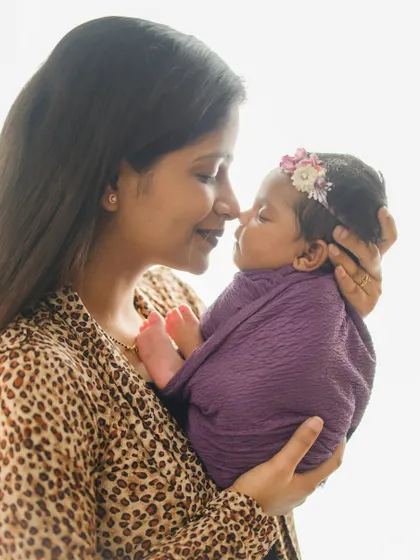 A mother's love, reflected in her soft smile as she holds her baby close. The delicate floral headband adds a sweet touch to this tender portrait.