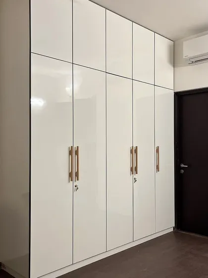 A sleek, high-gloss white wardrobe with custom wooden handles, part of a budget-friendly full home interior project.