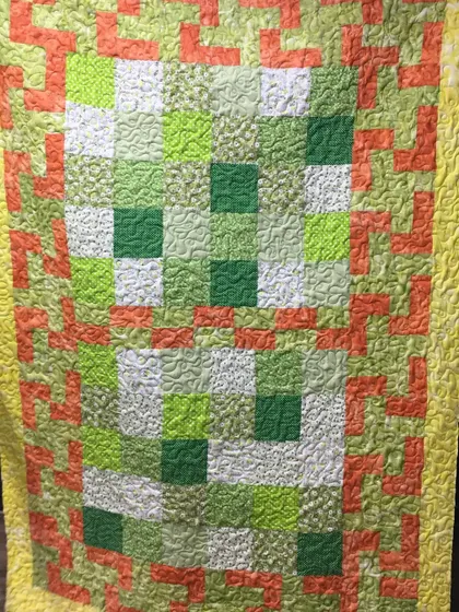 A modern quilt in fresh greens and oranges with a geometric border.