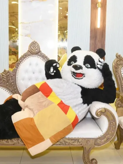 The panda mascot strikes a relaxed pose on a couch, adding a humorous touch to the event photos.