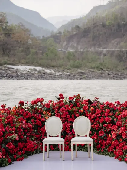 Another perspective of the riverside ceremony, showing the dramatic contrast between the red flowers and the majestic, earthy tones of the mountains. A truly unforgettable setting for vows.