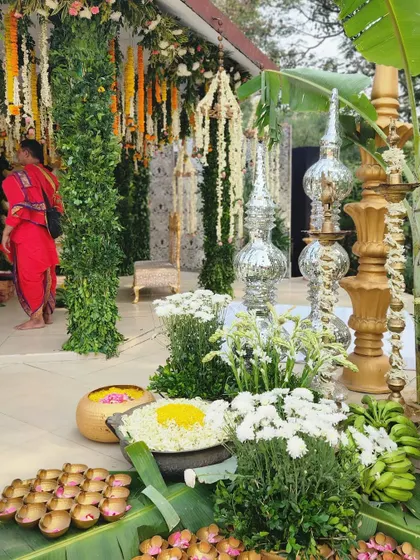 Embracing tradition with hues of gold and green. This corner of a South Indian wedding features tall diyas, silver lamps, and bowls of flowers set on banana leaves, creating a culturally rich and graceful display.