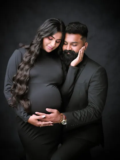 A moody and intimate low-key portrait. The dark background and focused lighting draw all the attention to the couple's connection and the beautiful baby bump.