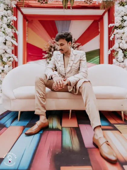 A stylish groom posing on a couch at the carnival-themed event.
