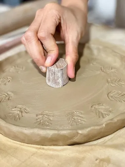 In our one-day workshop, you can learn to make and decorate your own plate. Here, a student is imprinting a pattern onto their hand-built plate.