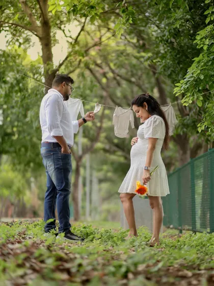 A creative and sweet outdoor scene. The couple is setting up a clothesline with baby clothes and an ultrasound picture, a lovely visual story of their preparation and excitement.