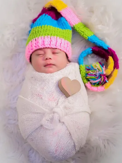 A swaddled newborn wearing a colorful knitted hat, with a small wooden heart placed on their chest. A simple and sweet way to capture newborn love.