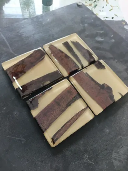 A set of modern coasters where pieces of dark wood are set in a creamy, opaque resin. The clean lines and neutral colors make them suitable for any decor style.