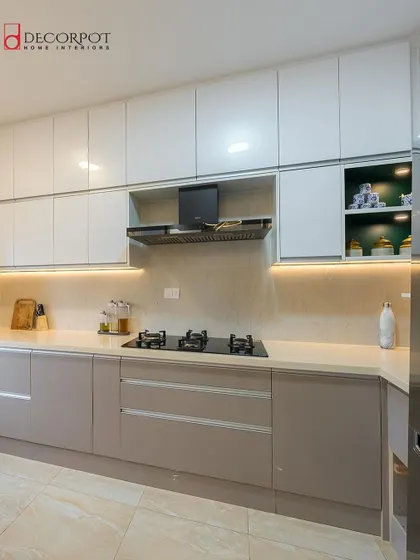 A clean and modern L-shaped kitchen with two-tone cabinets in light grey and white. The handleless design and under-cabinet lighting contribute to the sleek, minimalist aesthetic.