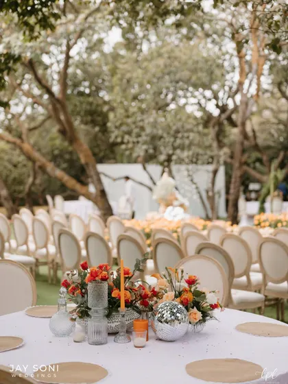 A table centerpiece with orange flowers and a disco ball, looking out towards the ceremony seating, tying all the event spaces together.
