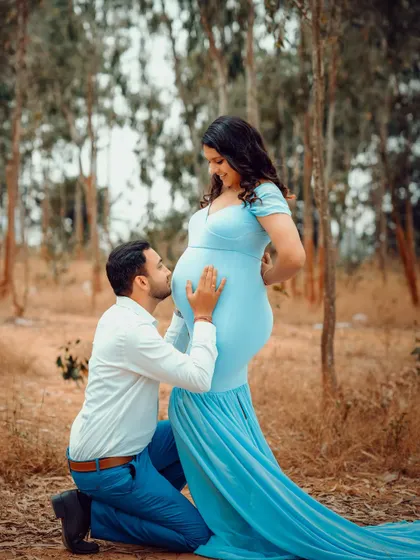 The dad-to-be kissing the baby bump is a classic and heartwarming pose, made even more beautiful by the natural outdoor setting.