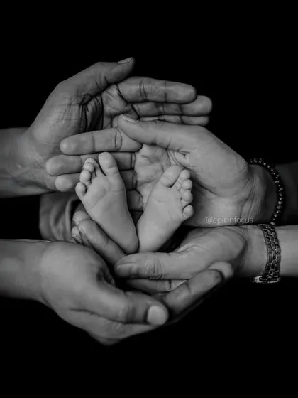 A timeless black and white photograph showing a newborn's tiny feet held securely in the hands of their family. We focus on these small, precious details that tell a big story of love and connection.