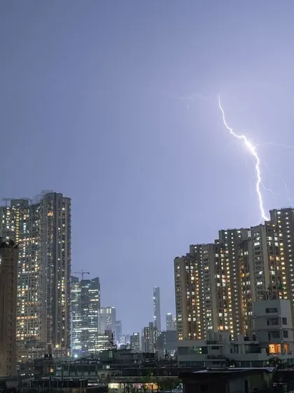 A powerful lightning bolt illuminates the clouds as it strikes down behind a building in Mumbai.
