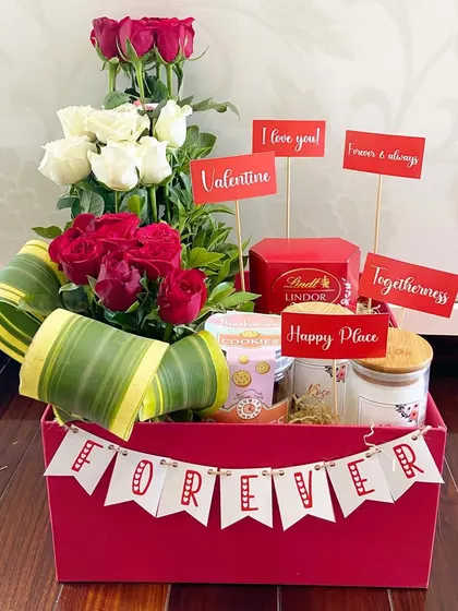 A classic Valentine's hamper with a personal touch. This arrangement includes a dozen red and white roses, a 'Forever' banner, and cute message cards, along with a scented candle and gourmet treats.