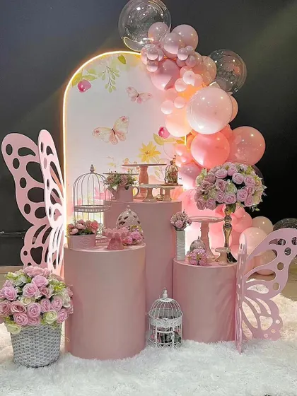 I create custom party decor for at-home birthdays, like this enchanting butterfly theme. The setup features pink pedestals for the cake, butterfly wing cutouts, and beautiful floral arrangements.