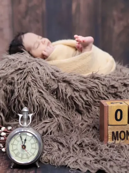 A one-month milestone photo featuring a newborn sleeping peacefully next to a vintage clock and calendar blocks. We have many props to mark these special dates.