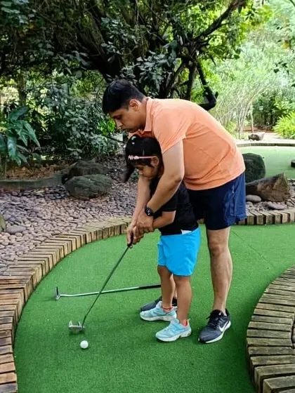 A father teaches his daughter how to play mini-golf. These are the quiet, patient moments of connection that families cherish.