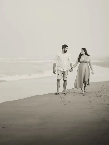A classic walking shot of Milando and Joann on the beach, rendered in a soft, sepia-toned black and white for a nostalgic, film-like quality.