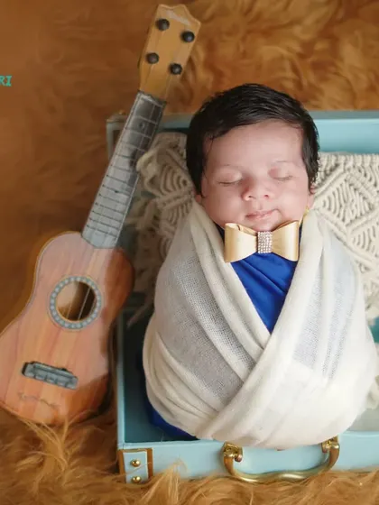 A little musician in the making. This newborn is posed in a vintage-style suitcase with a tiny guitar, showcasing a creative and personalized setup.