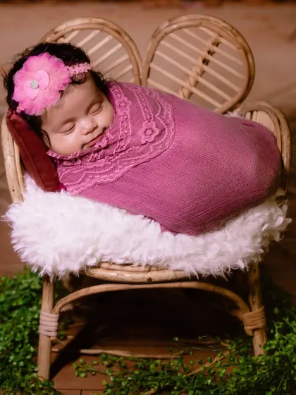 Cozy and content in a miniature cane chair. This newborn girl is wrapped in a soft pink blanket, showcasing a simple and sweet prop setup.