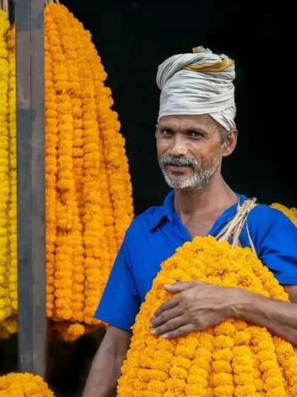 A flower seller at a Delhi market, surrounded by garlands of yellow and orange marigolds. His tired smile tells a story of a long day's work.
