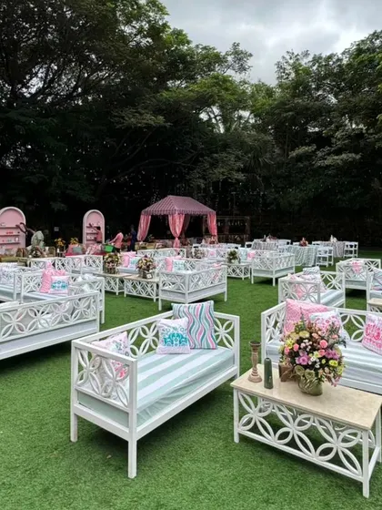 A whimsical lawn setup for a 'Tale of Two Souls' themed event, with rows of white benches adorned with custom-printed pastel cushions.