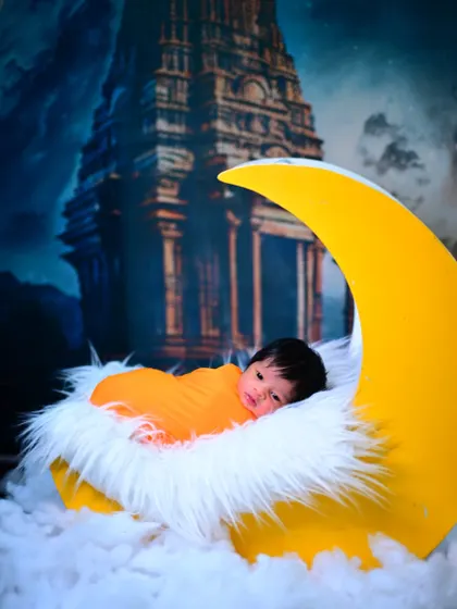 A magical newborn photo with the baby nestled in a crescent moon prop, set against a celestial backdrop with a temple.
