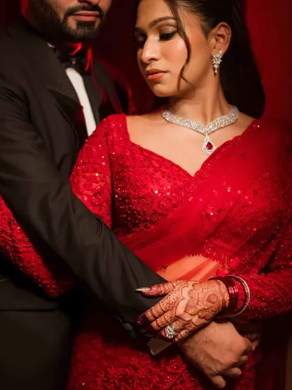 A close-up detail shot from the reception portrait session. The focus is on their intertwined hands, the bride's intricate henna, and her sparkling red saree.