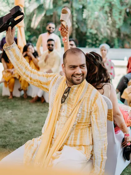 The groom playfully holds up shoes during a traditional game at the Haldi ceremony.