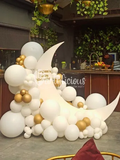 Over the moon for this baby shower setup. A crescent moon prop adorned with white and gold balloons creates a dreamy photo corner.