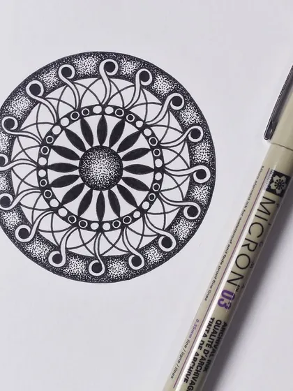 A circular mandala design created with a Micron 03 pen. The pattern uses repeating swirls and stippling to create a sense of movement and depth.