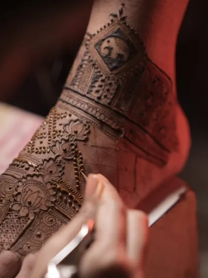 Another view of the bridal foot mehendi, showing the combination of the elephant band and a delicate lotus pattern being drawn on the top of the foot.