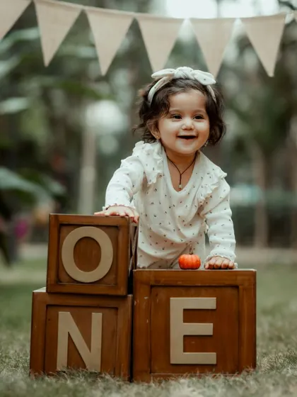 A duplicate of image 10, showing a joyful first birthday portrait of a baby girl with "ONE" blocks in an outdoor setting.