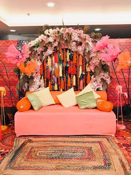 A full view of the vibrant Mehendi stage setup. I used a rich, patterned backdrop, a comfortable diwan, and colourful props like floral umbrellas and flamingo figures to create a lively, bohemian vibe.