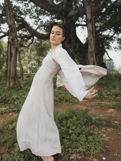 A full-body shot from 'SOLARA' showing the elegant drape of the dress and jacket. The pose is fluid and expressive, interacting with the natural surroundings.
