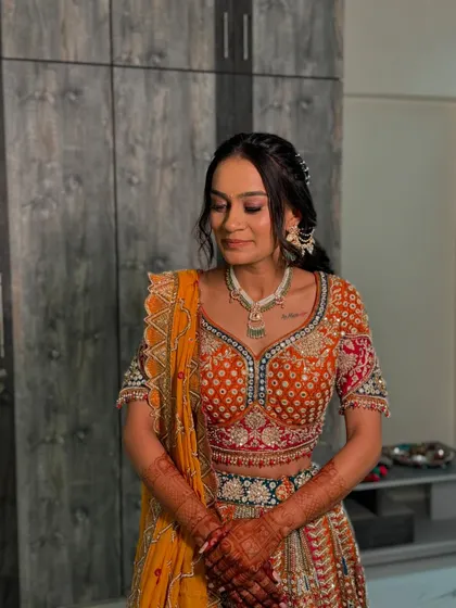 The bride looking down, showcasing her soft and warm-toned eye makeup that perfectly complements her colourful orange and yellow lehenga.