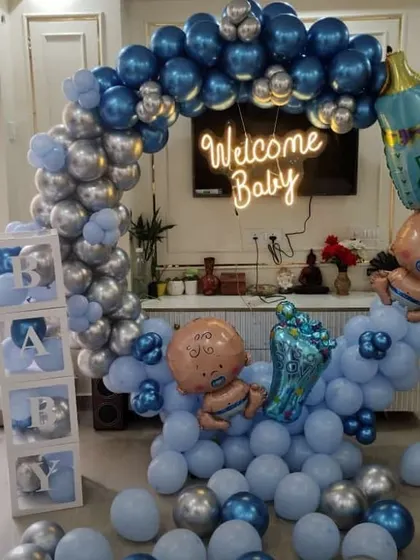 A full "Welcome Baby" boy setup in a living room. It features a balloon ring in shades of blue and silver, "BABY" blocks, and cute baby-themed foil balloons.