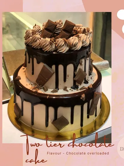 A stunning two-tier chocolate drip cake, topped with chocolate chunks and swirls. This is a perfect centerpiece for any party.