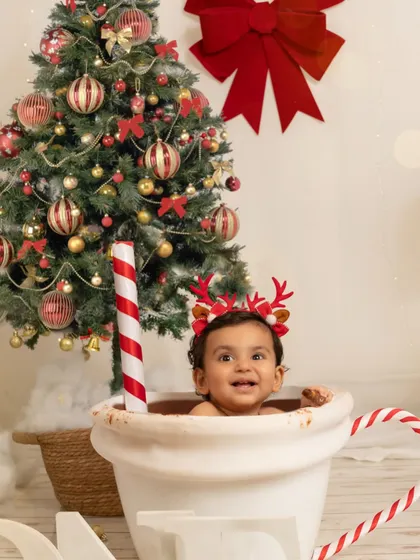 A close-up of the baby's happy face as he sits in the mug, wearing reindeer antlers, perfectly capturing the joy of his first Christmas.