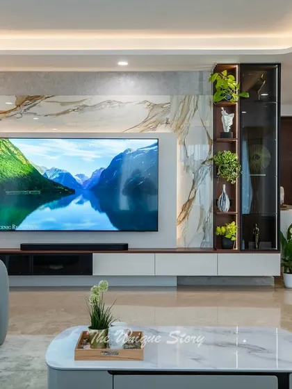A close-up of the living room's TV unit, featuring a book-matched marble panel and a vertical display niche. The combination of natural stone, warm lighting, and greenery adds a touch of biophilic luxury.