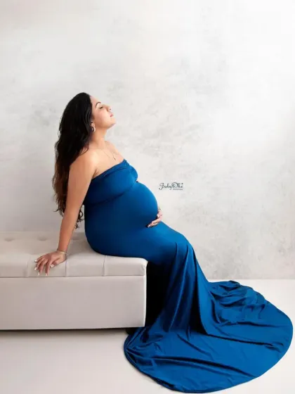 A moment of pure bliss. This artistic side profile of the mom-to-be in a blue mermaid gown highlights the beautiful silhouette of pregnancy against a textured, minimalist backdrop.