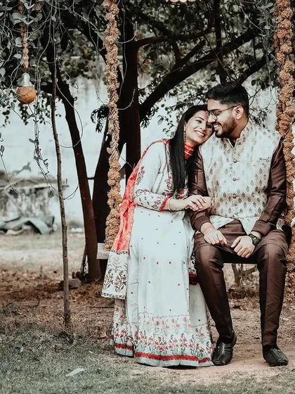A quiet, candid moment during a pre-wedding shoot. The couple sits together on a rustic swing, sharing a laugh in a natural, unposed interaction that reflects their genuine connection.