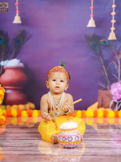 A classic pose for a Bal Krishna photoshoot, sitting with his flute and a pot of butter. The purple background adds a touch of royalty to the scene.