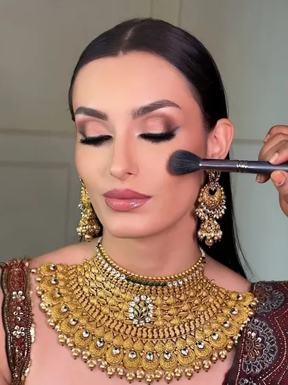 A behind the scenes moment, applying a soft blush to add warmth to the cheeks. This step is crucial for bringing life to the face and ensuring the makeup looks dimensional on camera for this traditional jewelry shoot.