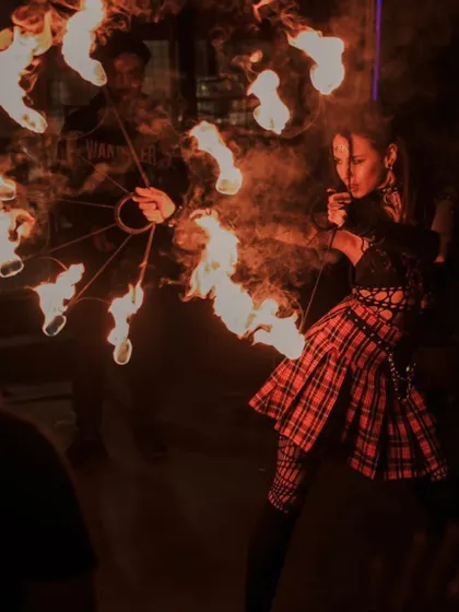 A female artist performs with circular fire fans, a prop that creates large, impressive wheels of fire. Her punk-inspired costume adds to the edgy vibe of the show.